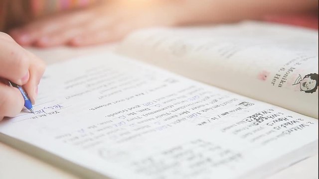 The girl at the table writes with a ballpoint pen in a notebook task in English