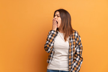 Young woman over brown wall yawning and covering wide open mouth with hand