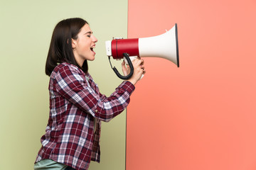 Young woman over isolated colorful wall shouting through a megaphone