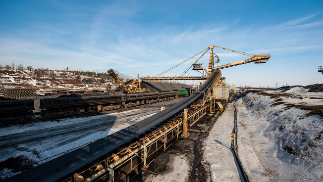 delivery of iron ore by a conveyor belt from a warehouse and loading into railway dump cars.