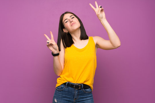 Young woman over isolated purple wall showing victory sign with both hands