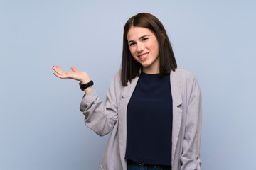 Young woman over isolated blue wall holding copyspace imaginary on the palm to insert an ad