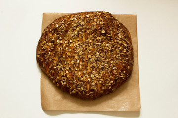Tasty whole pie on parchment paper with grains and seeds on top on white background