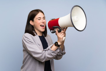 Young woman over isolated blue wall shouting through a megaphone