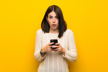 Young woman over isolated yellow wall surprised and sending a message