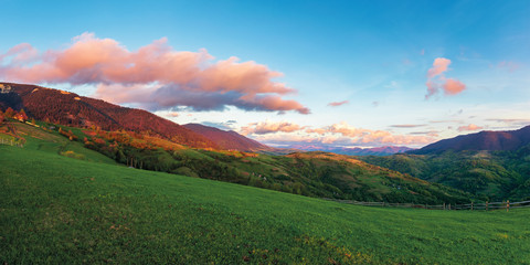 beautiful rural panorama in mountains at sunset. agricultural fields on hills. ridge in the distance. fence along the pasture. wonderful carpathian countryside in springtime. blue sky with red clouds.