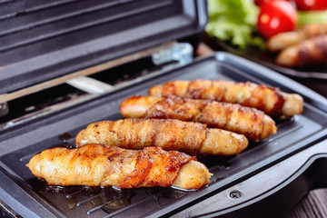Appetizing sausages wrapped in bacon are grilled on a electric grill