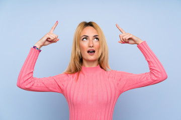 Young blonde woman with pink sweater over isolated blue background pointing with the index finger a great idea