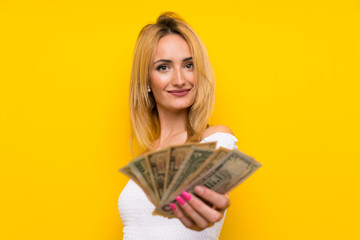 Young blonde woman over isolated yellow wall taking a lot of money