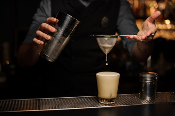 Bartender pours cocktail using sieve and shaker