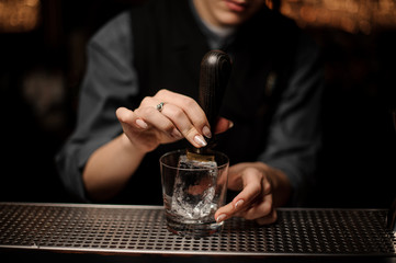 Bartender adds ice in glass with an ice pick