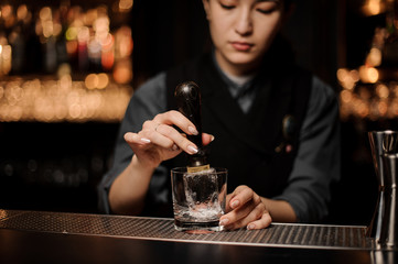 Bartender adds ice in glass with an ice picker