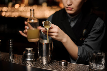 Female bartender pouring cocktail with sour mix in a shaker
