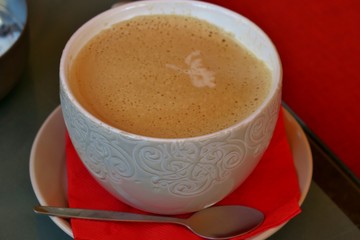 coffee in a white cup with a pattern on a saucer with a red napkin