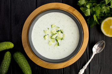 Yogurt smoothies  with  cucumber in the dark bowl  on the black wooden background.Top view.