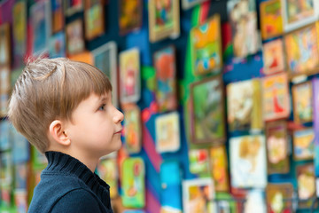 The boy looks at the paintings at the exhibition of pictorial art and creativity.