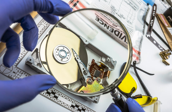 Police expert examines with magnifying glass hard drive in search of evidence, conceptual image