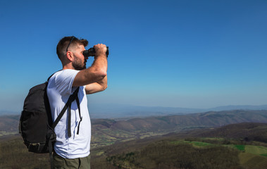 Hiker with backpacks observes the panorama on top of a mountain with binoculars