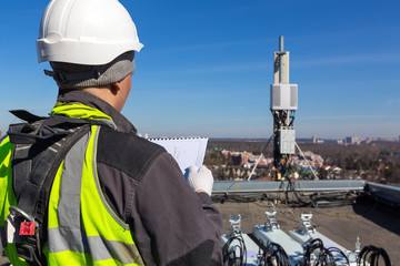 Professional industrial climber in helmet and uniform reads technical documentation and antennas of...