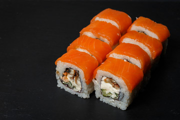 Philadelphia roll sushi with salmon, avocado, cream cheese served on black stone slate