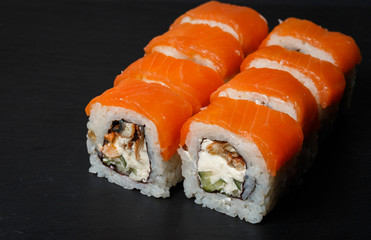Philadelphia roll sushi with salmon, avocado, cream cheese served on black stone slate