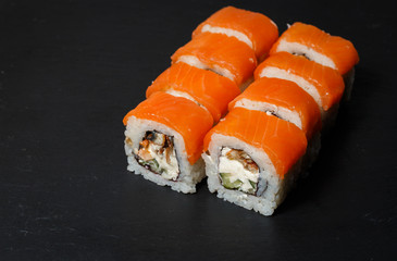 Philadelphia roll sushi with salmon, avocado, cream cheese served on black stone slate