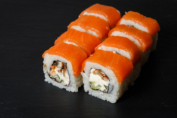 Philadelphia roll sushi with salmon, avocado, cream cheese served on black stone slate