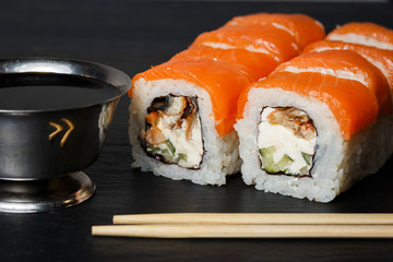 Philadelphia roll sushi with salmon, avocado, cream cheese served on black stone slate