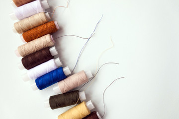 Row of number of different colors colorful multicolored sewing thread spools on light blue background. Selective soft focus, text copy space.