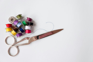 Number of different colors colorful multicolored sewing thread on metal spools with metal scissors on light blue background. Selective soft focus, text copy space.