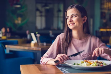 Zelfklevend Fotobehang Young woman smiling and looking away while eating lunch at the restaurant © eshana_blue