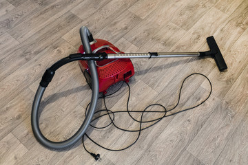 Red vacuum cleaner with electric cable laid out on the linoleum floor