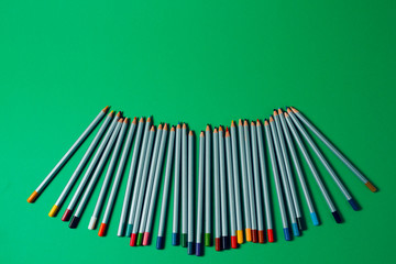 colored pencils arranged in a chaotic line on green background