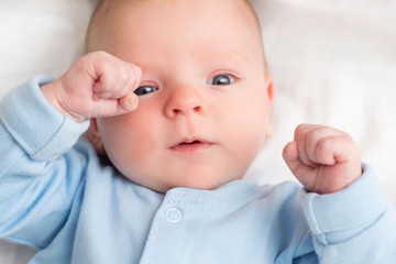 Baby lying down on back, happy toddler in bodysuit looking up. Portrait of a cute baby lying down on a bed, top view