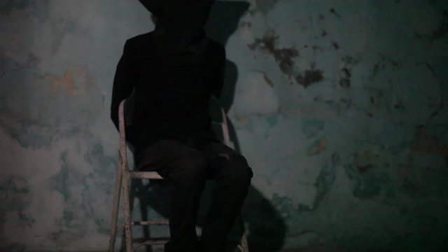 Male human wearing a black colored mask and black attire tied hands and sitting on the metal chair. Kidd napping concept.