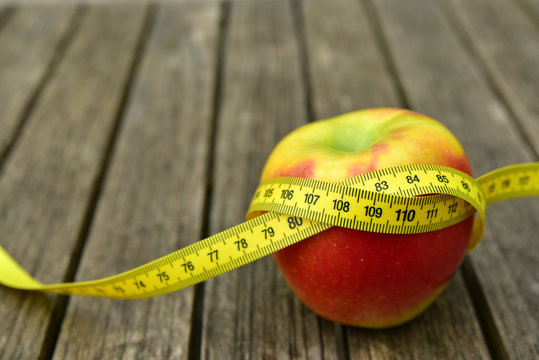 roter apfel auf einem holztisch mit einem ma&szlig;band darum