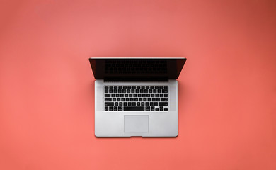 Laptop on pale red background overhead view
