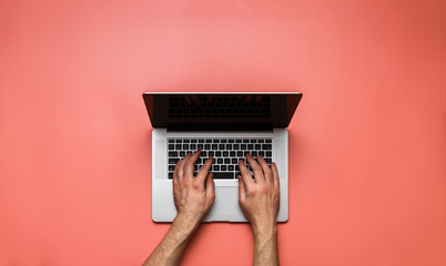 Fototapeta na wymiar Man hands using laptop on pale coral color desk