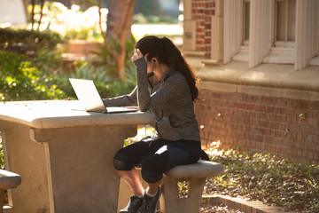 A female college student works on her laptop in the morning sun