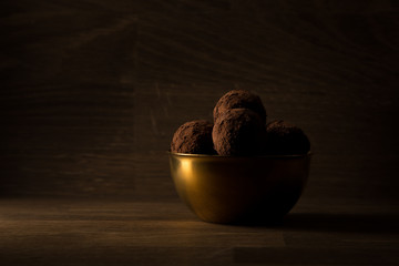 dark chocolate truffles in golden bowl on wooden background, golden light, copy space