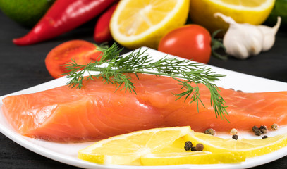 .slice of red fish with lemon and fruit on a black background