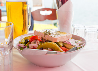 Bowl of fresh greek salad with feta cheese, green pepper, tomato, cucumber, olives and red onion. Beer mug and empty glasses on table
