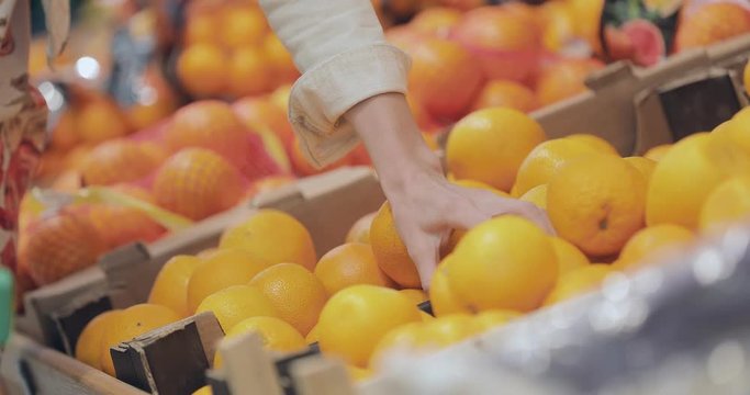 Girl gets an orange from the box from the supermarket shelf. Span of the camera on the shelf with fruit.