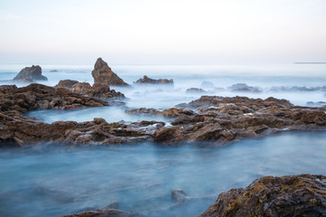 Long exposure fluffy ocean mists rush over tidal pool rocks at the beach