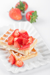 Belgium waffers with sugar powder and strawberries on ceramic plate on white table.