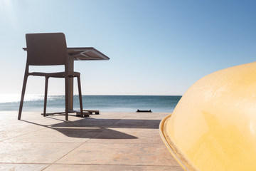 Upside down yellow boat, table and chair on the pier by the sea in the early summer morning.