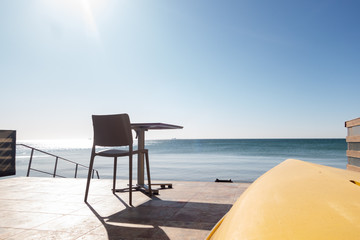 Upside down yellow boat, table and chair on the pier by the sea in the early summer morning.