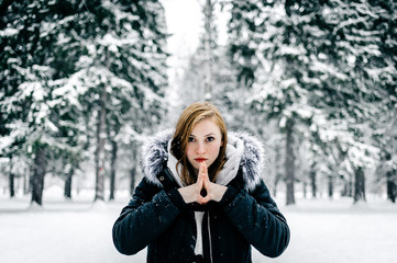 Fototapeta na wymiar Portrait of a beautiful girl in the black jacket with fur hood amid winter forest