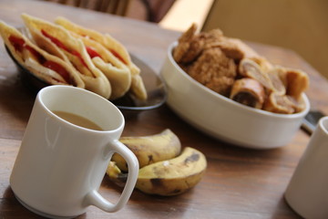 breakfast with a white cup of tea on a background of bananas, sandwiches and sweets in a plate