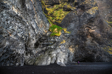 Couple on a Black Sandy Beach at the Bottom of a Steep Basalt Cliff in Iceland